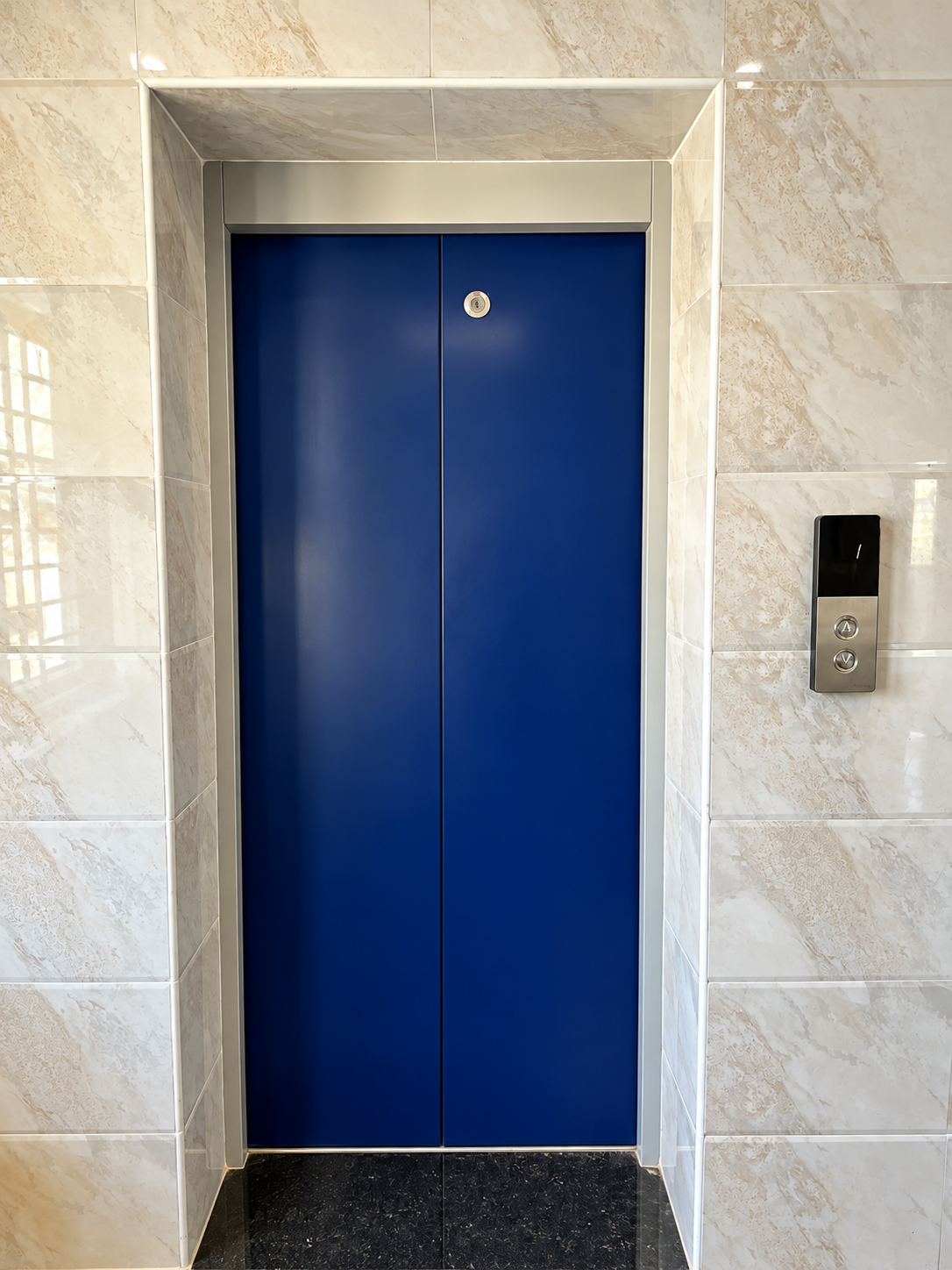 Fine Dine Academy lift entrance with blue doors beside marble tiled walls
